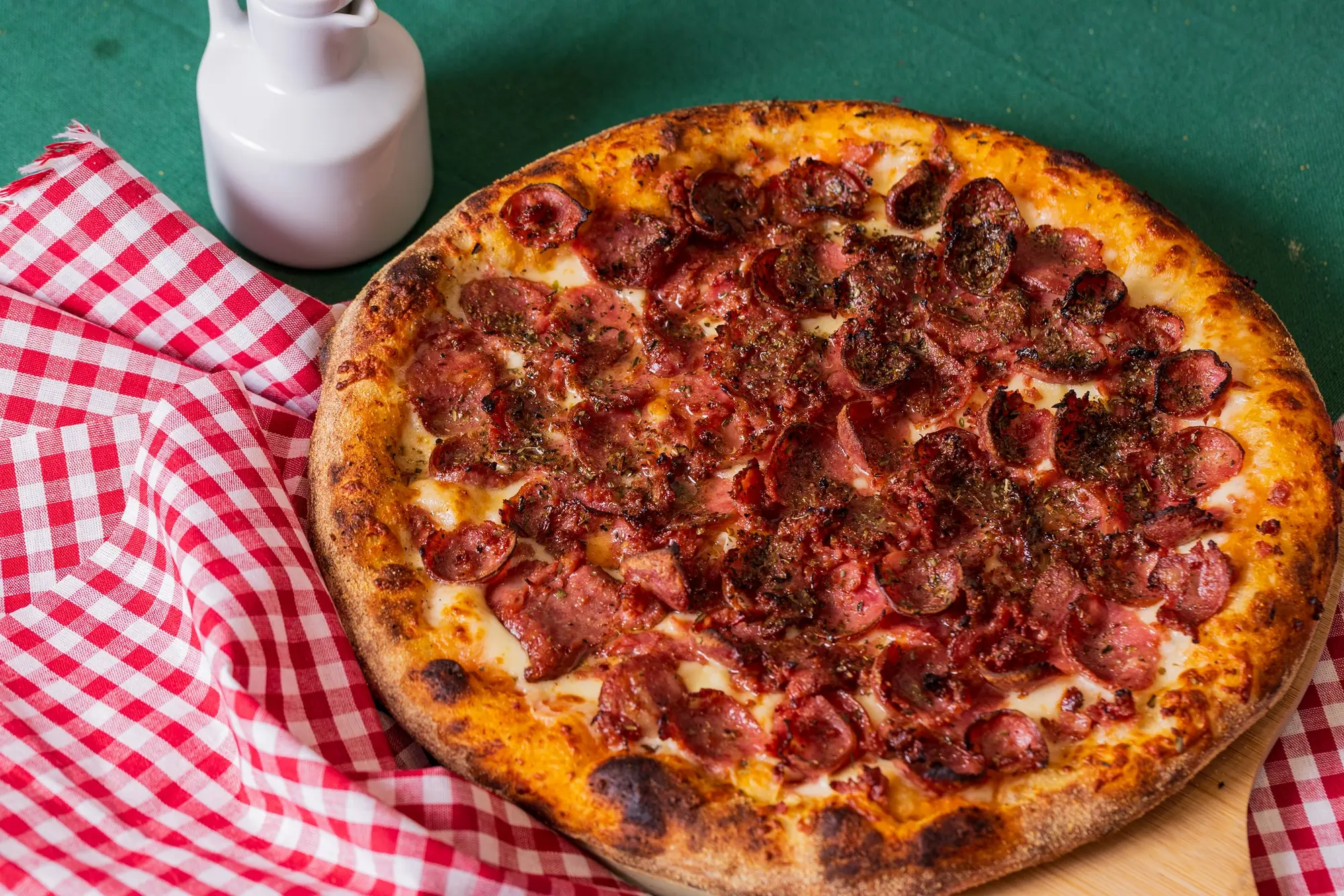 Pizza de calabresa inteira sobre a tábua, na mesa de toalha xadrez