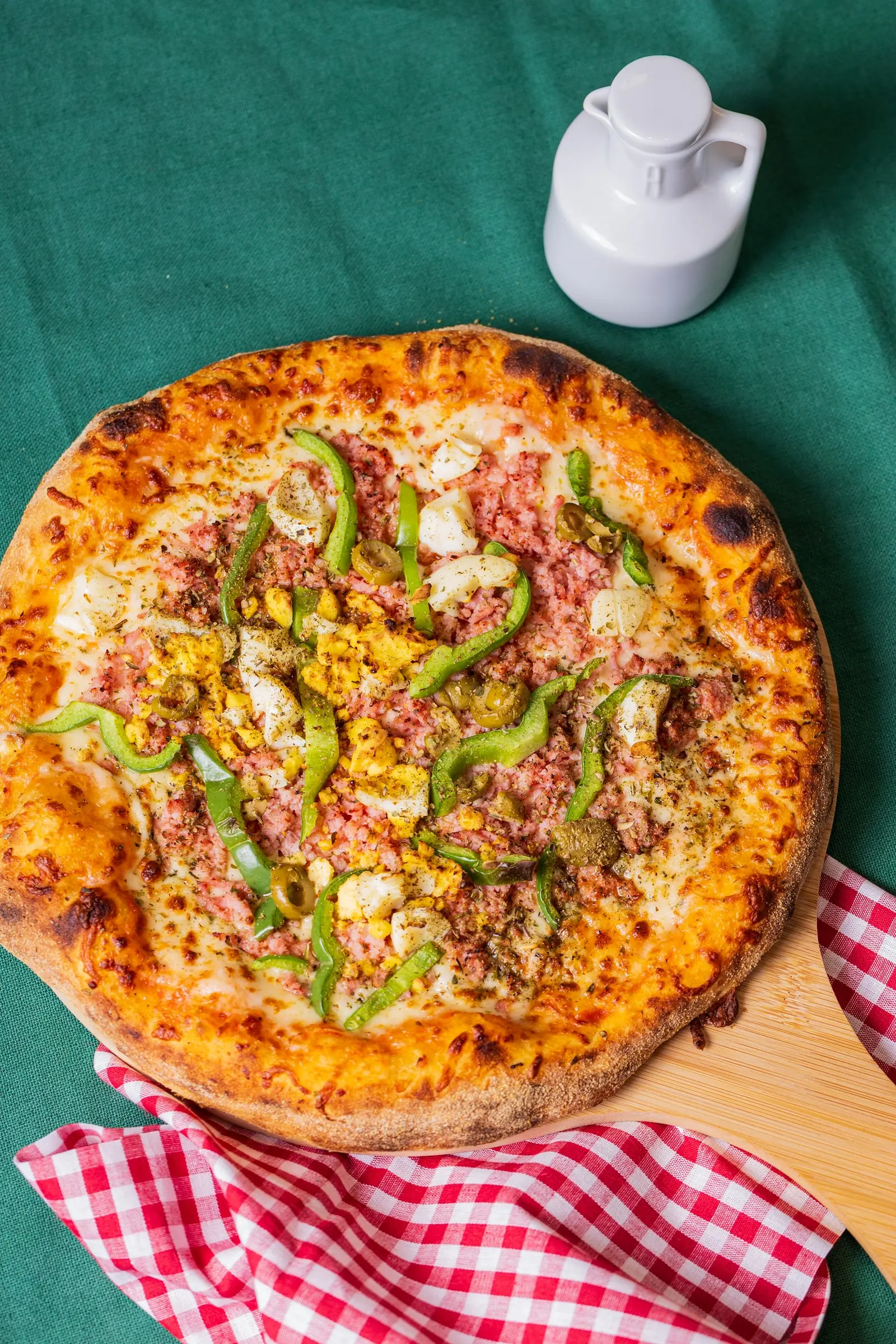 Pizza portuguesa inteira com pimentão verde, sobre a tábua